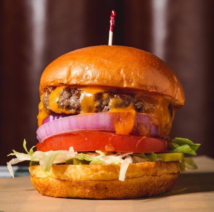 Rodeo Goat DCC burger with melted cheese, red onion, tomato, lettuce, and pickles